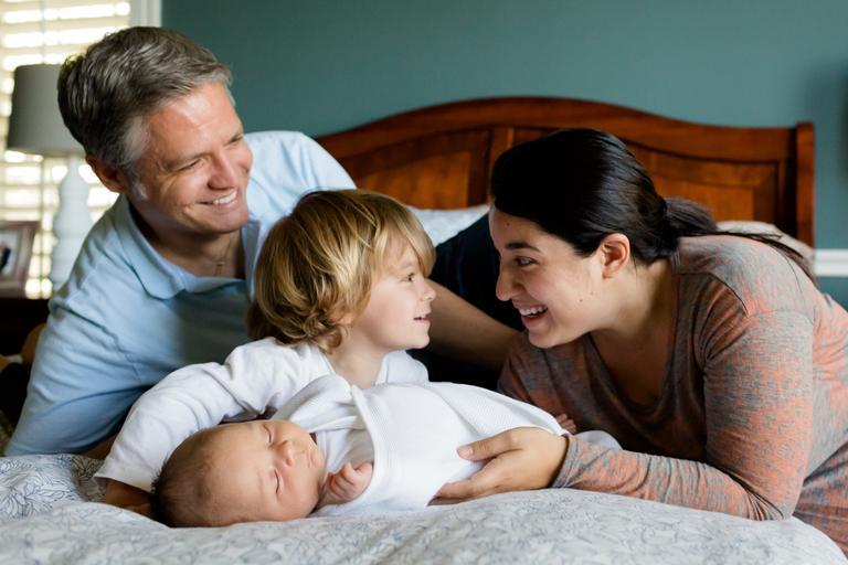 Parents, child, newborn on a bed laughing and smiling